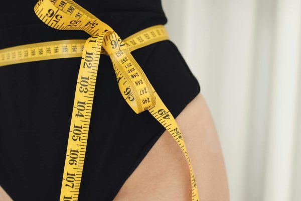 Woman measuring waist with tape measure for body contouring results